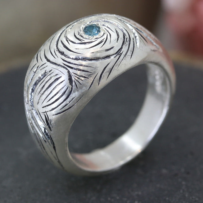 Silver ring with intricate design and blue gemstone on a dark surface