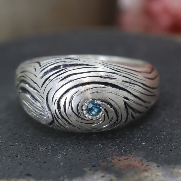 Silver ring with a blue gemstone on a dark surface