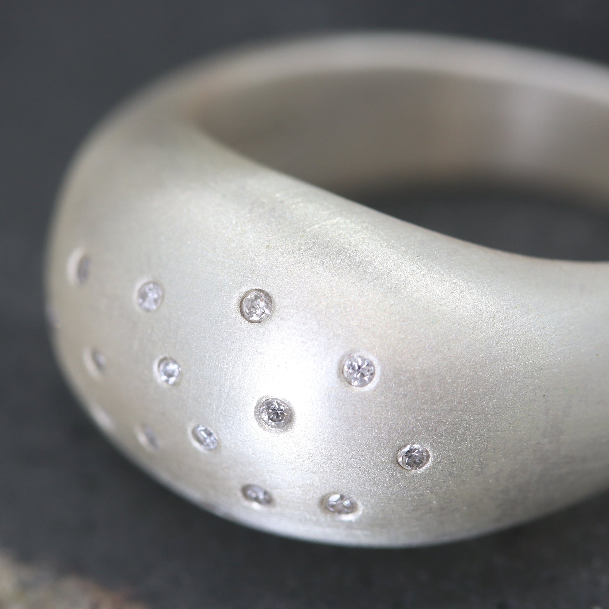 Silver ring with embedded diamonds on a textured surface