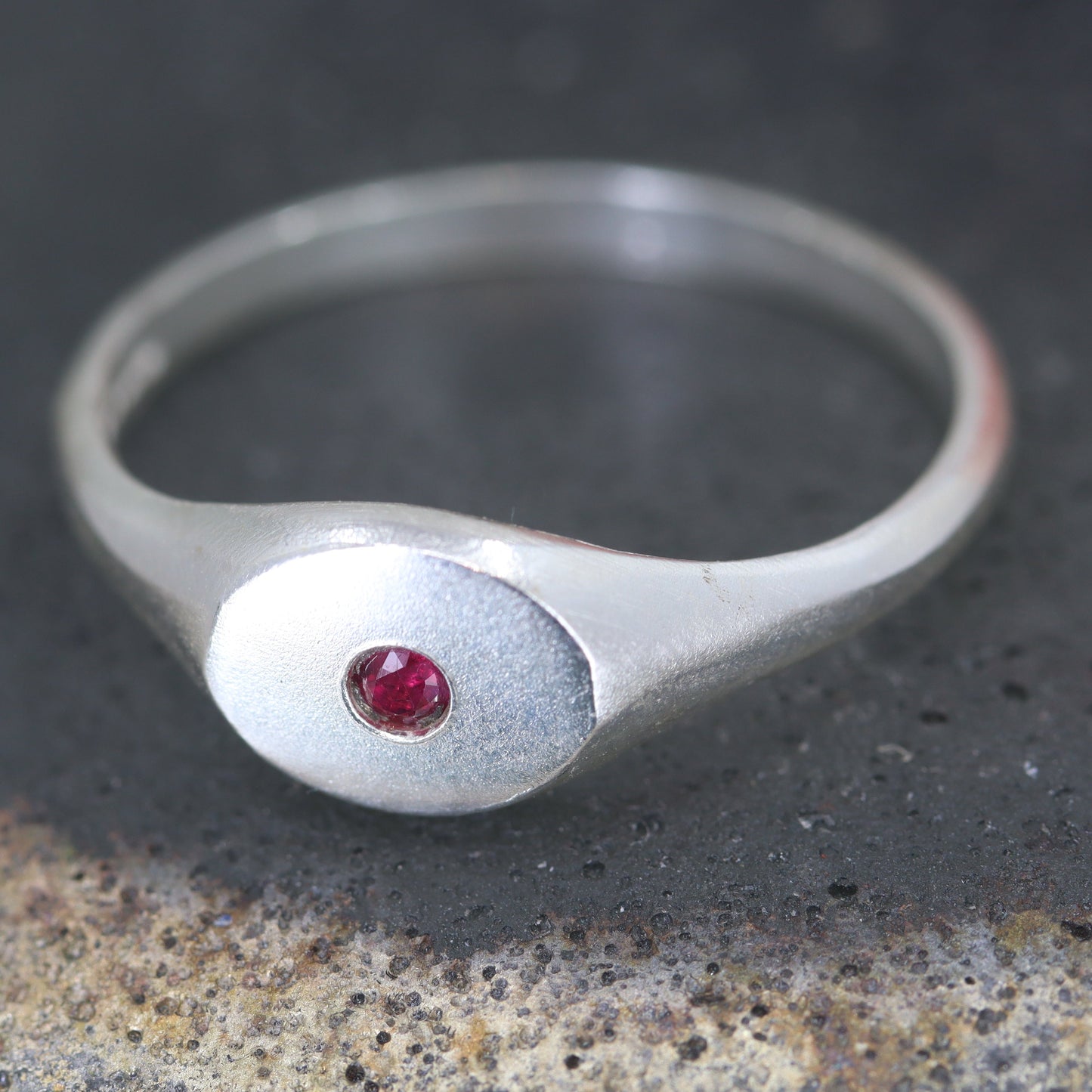 Silver ring with a ruby gemstone on a textured surface